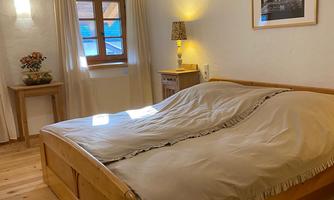 A cozy bedroom with a wooden bed and soft blankets. The light shines through the window, creating an inviting atmosphere.
