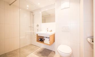 A modern bathroom with a glass shower and a simple sink. The walls are brightly tiled, creating a friendly atmosphere.