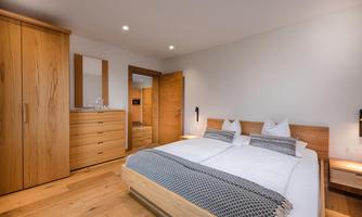 A modern bedroom with a double bed and wooden furniture. The walls are bright and the room is well-lit.
