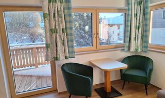 A cozy living area with two chairs and a small table. Through the windows, you can see a snowy outdoor area.