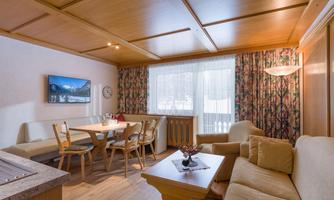A cozy living kitchen with wooden ceilings and large windows. A dining area with a table, chairs, and a sofa invites you to relax.