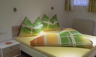 A quiet bedroom with a large bed, colorful cushions, and simple furniture design. The room has a bright and inviting character.