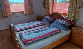 A cozy bedroom with a double bed and bright curtains. Large windows provide plenty of daylight and a view outside.