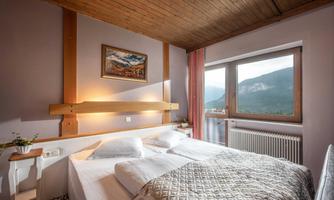 A cozy bedroom with a large bed and a window that offers a view of the mountains. The warm wooden ceiling and soft lighting create an inviting atmosphere.