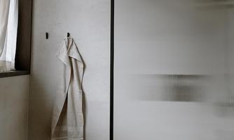 A modern bathroom with a glass shower and a towel on the wall. The colors are neutral, and the space feels minimalist and inviting.
