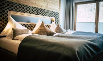 A stylish room with a large bed and cozy pillows. Large windows provide plenty of daylight.
