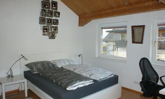 A cozy bedroom with a double bed and spacious windows. The walls are painted light, and the wooden ceiling creates a warm atmosphere.