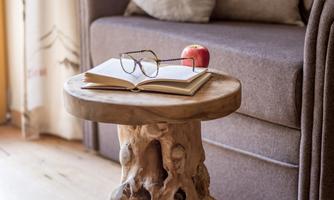 A cozy living area with a brown sofa and a unique wooden table. On the table lies an open book and a pair of glasses, next to it is a red apple.