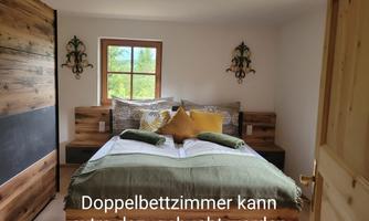 A cozy bedroom with a large bed and decorative pillows. A window overlooking greenery provides daylight and an inviting atmosphere.