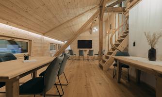 A modern room with wooden paneling and large windows. There are tables, chairs, and a staircase that leads to a second level.