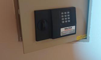 A wall safe with a combination lock and a keyhole. The safe is gray in color and is mounted on the wall.