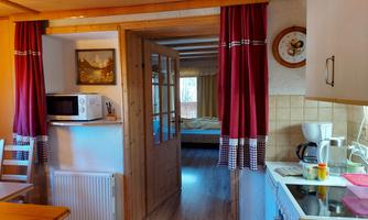 A cozy kitchen with wooden interior and red curtains. A bedroom is visible in the background.