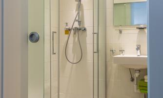 A modern bathroom with a glass shower cabin. There is a sink with a small mirror and bright lighting.