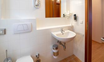A modern bathroom with white tiles and a small sink. There is a toilet, a mirror, and wooden doors.