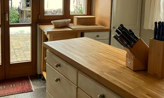 A modern kitchen with wooden worktops and a variety of kitchen knives. Large windows provide plenty of natural light and a view of the outdoor area.