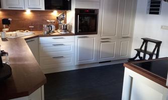 A modern kitchen with white cabinets and wooden details. The room is bright and well-equipped.