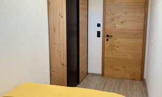 A modern bedroom with a large bed and a yellow throw. A wooden dresser and a wooden door complement the cozy atmosphere.