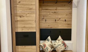 A modern piece of furniture made of wood with a cabinet, hooks, and a seating area. Two decorative cushions are placed on it.