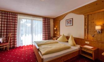 A cozy bedroom with wood interior and red carpet. The room features a large window overlooking a balcony and two beds with yellow pillows.