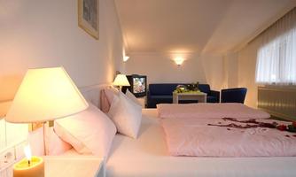 A cozy bedroom with a large double bed and soft pink bedding. The room features a television and a seating area that creates a relaxed atmosphere.
