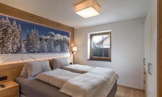 A modern bedroom with a double bed and wood paneling. On the wall is a large picture of snowy trees.