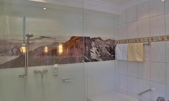 A modern bathroom with a glass shower and a bathtub. On the wall, there is a decorative mountain motif.