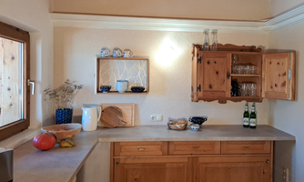 A cozy kitchen with wooden furniture and gentle lighting. Fresh groceries and some drinks are on the countertop.