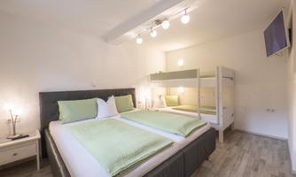A modern room with two beds and a loft bed. The decor is bright and friendly, with green cushions and plenty of natural light.