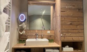 A modern bathroom with wood paneling and a sink on a wood shelf. In the background, there is a large mirror and fresh towels.
