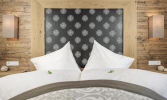 A cozy bedroom with a wooden frame bed and an elegant headboard. The white bedding is complemented with decorative cushions.