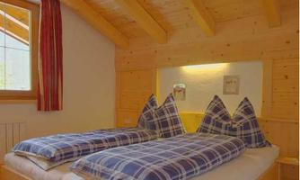 A cozy bedroom with a wooden ceiling and two single beds. The pillows have a checkered pattern and the walls are designed in a light color.