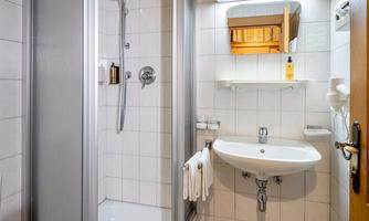 A modern bathroom with a shower, sink, and wooden ceiling. It is bright and clean, with white tiles and a towel rack.