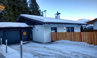A modern house in the snow with a wood exterior and a garage door. Snow-covered mountains are visible in the background.