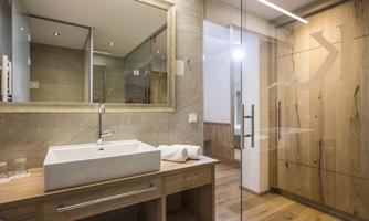 A modern bathroom with wooden details and a large mirror. The shower is made of glass, and the sink area is functional and stylishly designed.