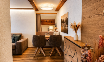 A cozy dining area with a wooden table and comfortable chairs. The walls are light and tastefully decorated, creating an inviting atmosphere.