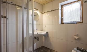 A modern bathroom with a shower cubicle, a sink, and a window. The walls are bright tiled and the furnishings are simple and functional.