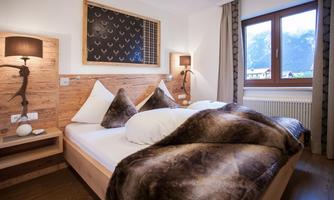 A cozy bedroom with a double bed and modern wooden furniture. Through the window, you can see the mountains, and the natural light creates an inviting atmosphere.