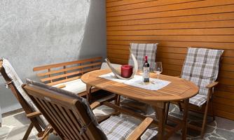 A cozy outdoor area with a wooden table and comfortable chairs. On the table, there is a glass of red wine and a bottle of wine.