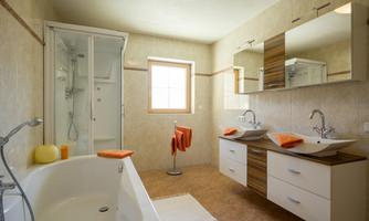 A modern bathroom with a walk-in shower and a bathtub. The walls are light, and orange towels provide an accent.