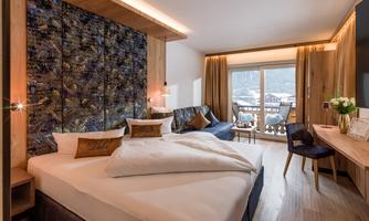 A modern hotel room with a large bed and a cozy seating area. A beautiful view of the mountains opens up to the balcony.
