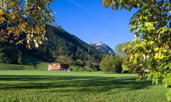 A beautiful valley with green meadows and high mountains. A farmhouse stands picturesque in the landscape.