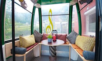 A cozy cabin with seating and a table in the middle. Colorful cushions and a plant create an inviting atmosphere.