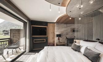 A modern bedroom with a large balcony and mountain view. The room is stylishly furnished with a comfortable bed and warm wood details.