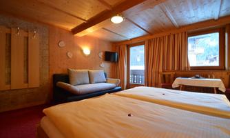 A cozy hotel room with two single beds and a comfortable sofa. Large windows allow natural light to enter and offer a view of the outside scene.
