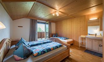 A cozy room with two beds and wooden paneling. The room has a balcony and a small washbasin.
