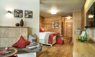 A modern hotel room with wood paneling and a cozy living area. The decor is stylish with red and gray accents.