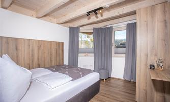 A modern bedroom with a double bed and wooden decor. Large windows and curtains provide daylight and coziness.