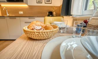 A beautiful dining table with a basket full of fresh croissants and a glass. In the background, a modern kitchen can be seen.