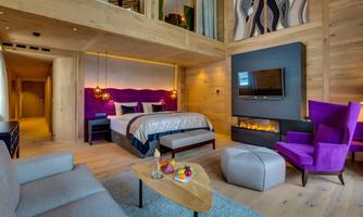 A modern room with wooden interiors, a large bed, and a seating area. The colorful accents create a cozy atmosphere.