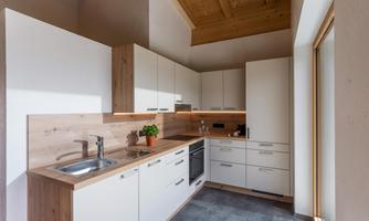 A modern kitchen with bright cabinets and wooden details. It has a bright atmosphere and large windows that let in a lot of light.